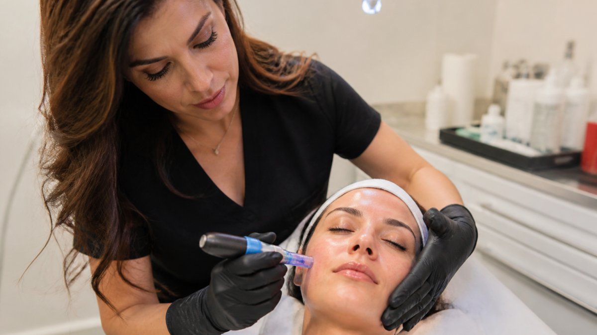 Professional aesthetician performing microneedling treatment on patient's face in clinical medical spa setting with soft professional lighting