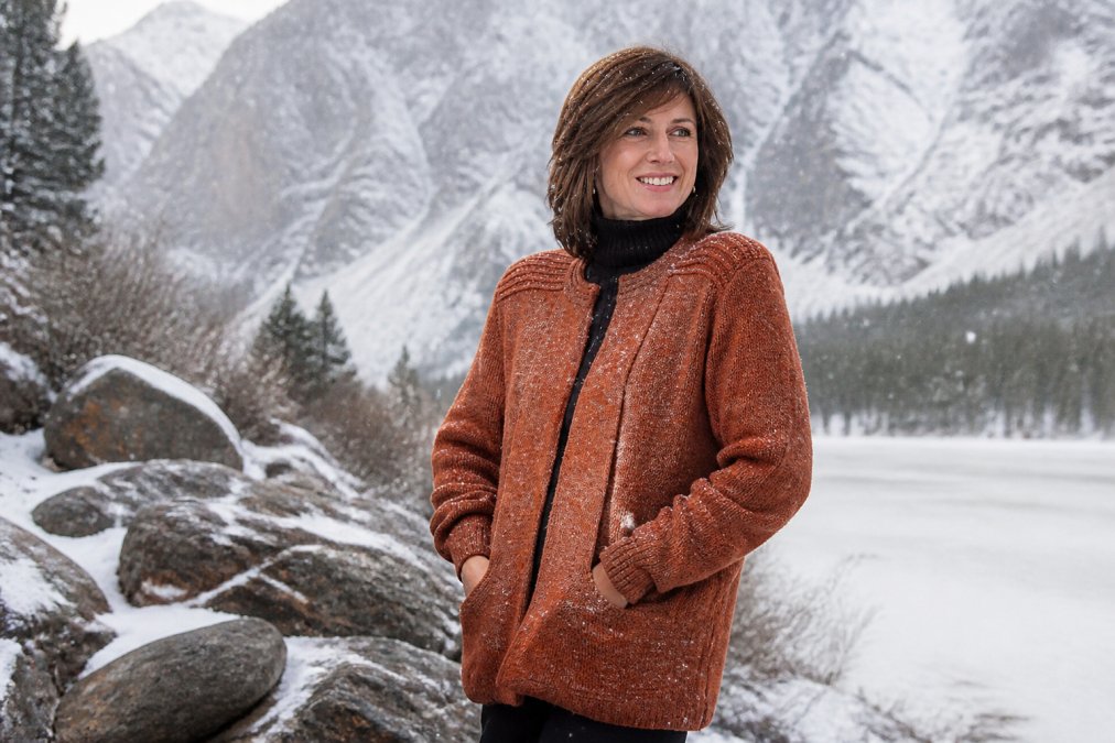 Person wearing an alpaca sweater outdoors in snowy mountain conditions, smiling comfortably while snowflakes fall, natural daylight