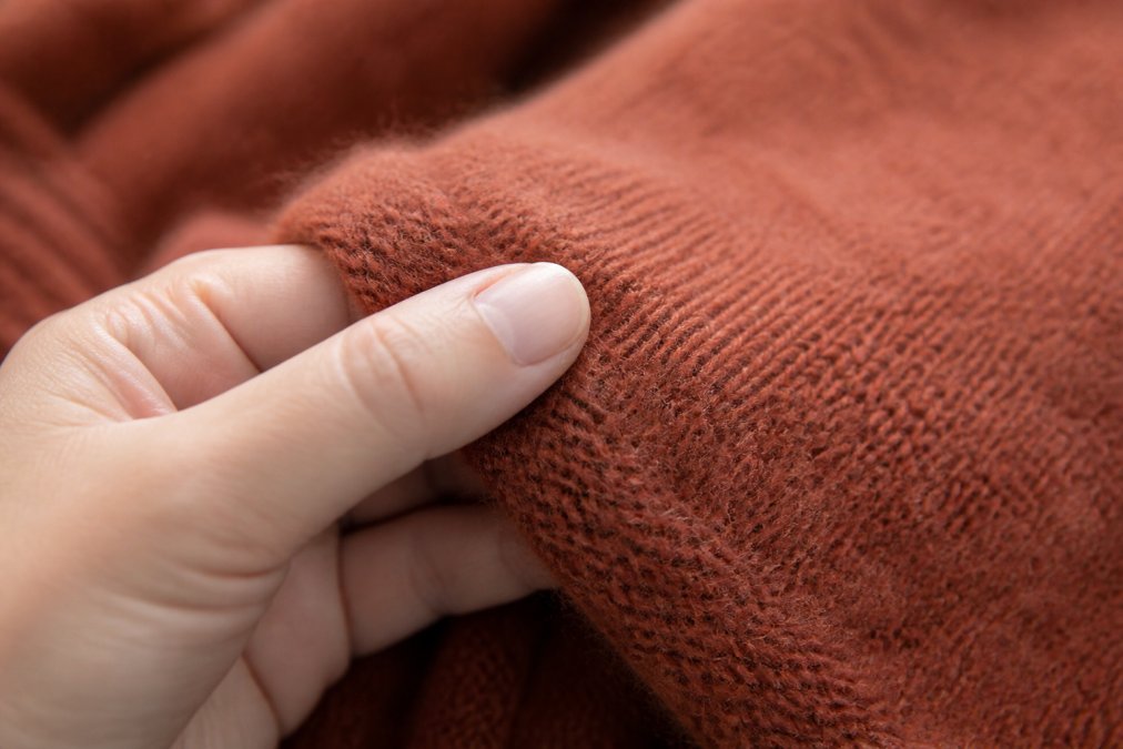 Close-up of soft alpaca fiber texture being gently held between fingers, showing fine smooth strands with natural light highlighting the fiber quality