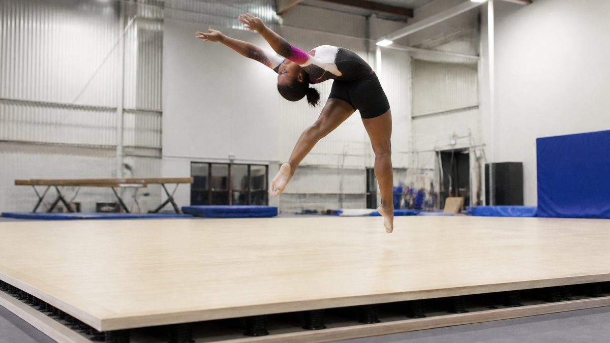 Athlete performing high-impact gymnastics move on professional Baltic birch sprung floor, showing dynamic floor response and stability during weight transfer