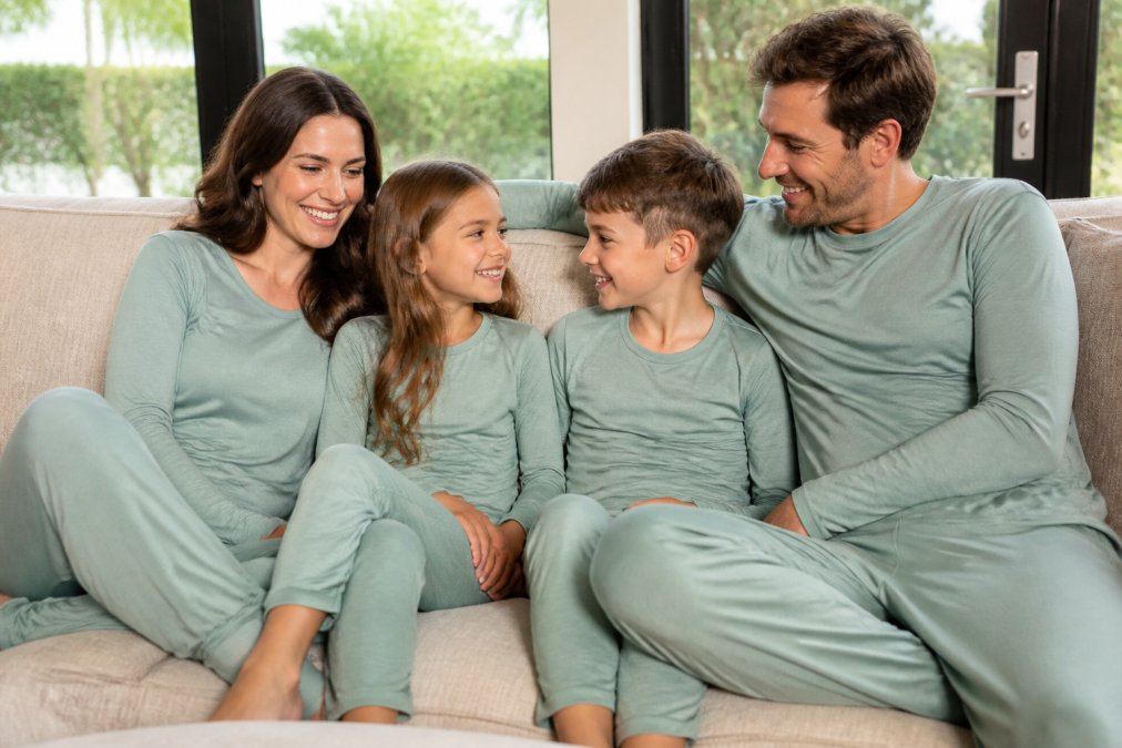 A family of four wearing matching bamboo loungewear, relaxing together on a couch in a bright living room, smiling and comfortable