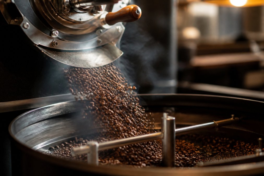 Freshly roasted coffee beans spilling from a small-batch roaster, capturing the rich aroma of local roasted coffee.