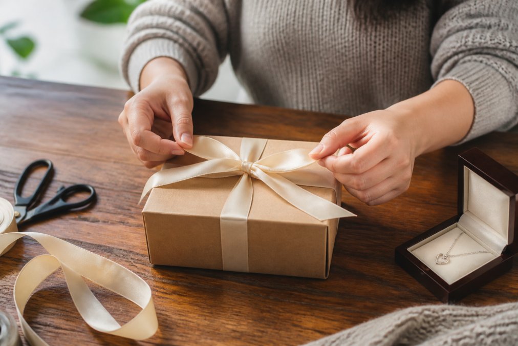 A person carefully wrapping a beautifully crafted personalized gift box on a wooden table, with soft natural light and a satin ribbon resting nearby, conveying deliberate care and thoughtfulness