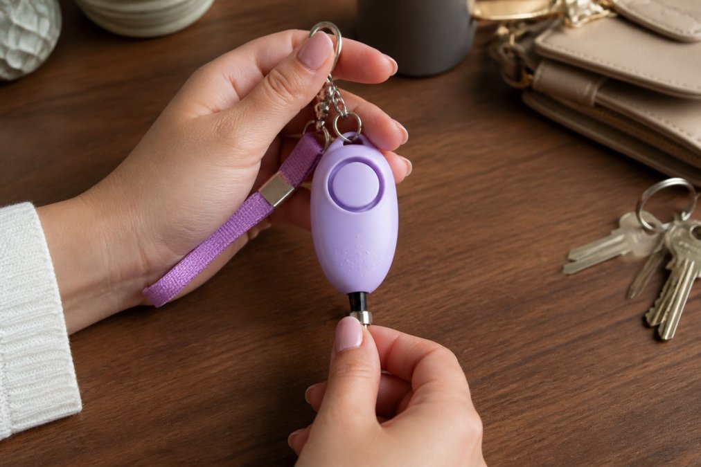 Close-up of hands holding a personal safety alarm keychain, demonstrating the activation button or pull-pin mechanism in a clear, accessible way