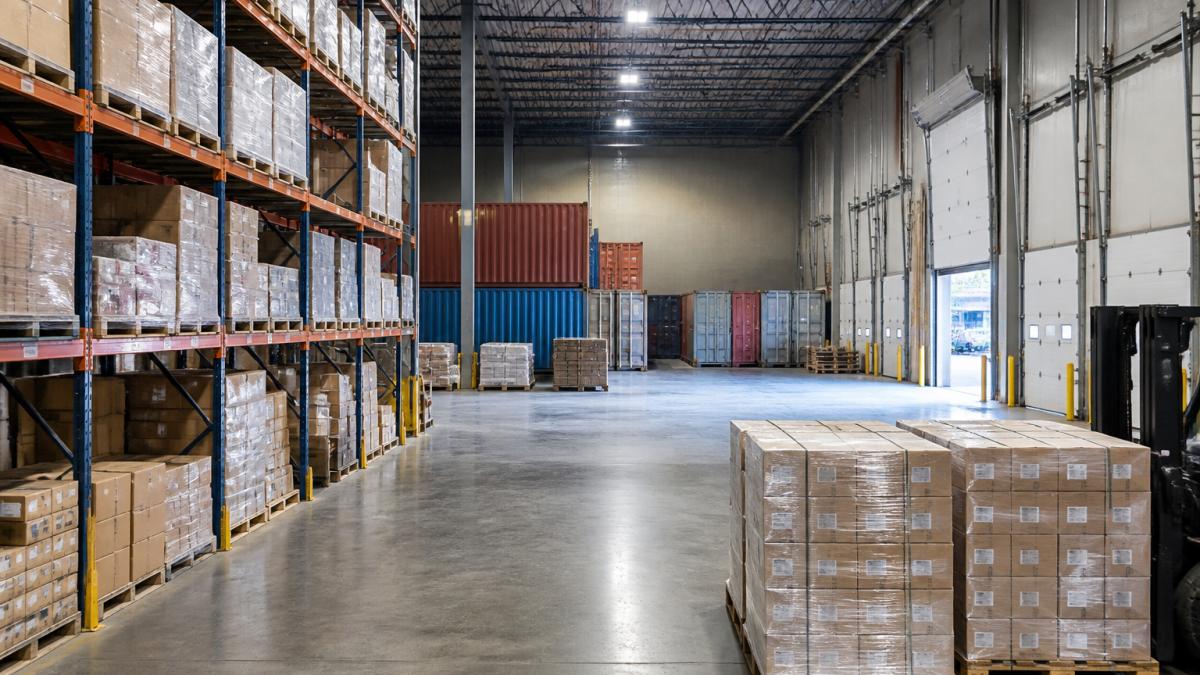 Wide view of a modern warehouse interior with organized inventory shelves, stacked shipping containers, and multiple dock doors showing the scale and security of a professional bonded storage facility
