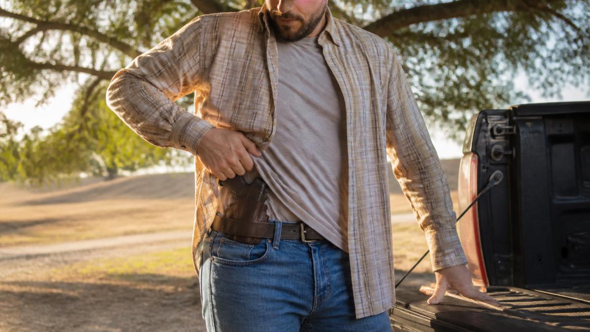 Person wearing custom leather IWB holster under untucked casual shirt, demonstrating natural concealment and comfortable body positioning during everyday activity