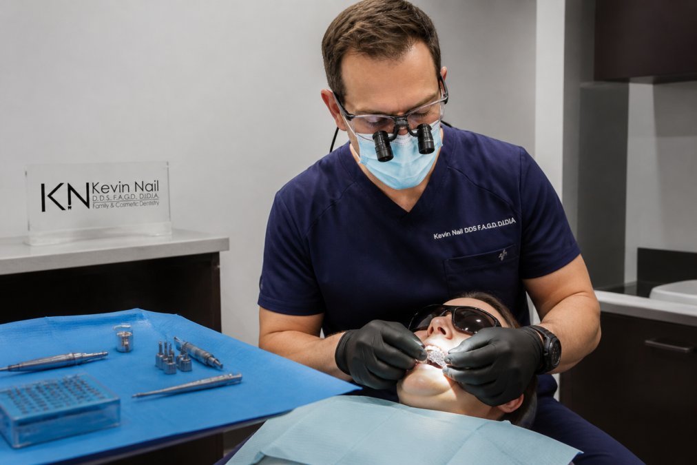 Close-up of a dental professional positioning a surgical guide template over a patient's lower teeth in a bright clinical operatory, with sterile implant instruments arranged on a covered tray beside the chair