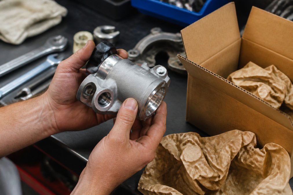 Close-up of hands inspecting an OEM part with visible hologram security feature, part number stamping, and original packaging with manufacturer branding in professional lighting