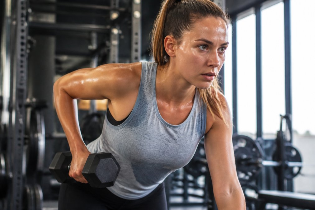 Athlete mid-workout in moisture-wicking activewear, visibly focused and energized, with sweat visible on the fabric surface but skin appearing dry and cool, performing an intense exercise in a bright gym setting