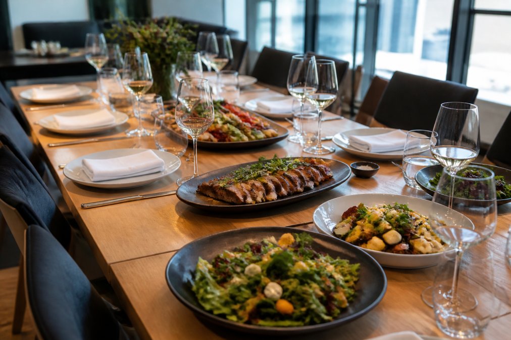 Beautifully set corporate dining table with fresh, gourmet dishes, wine glasses, and professional place settings in an office or home setting