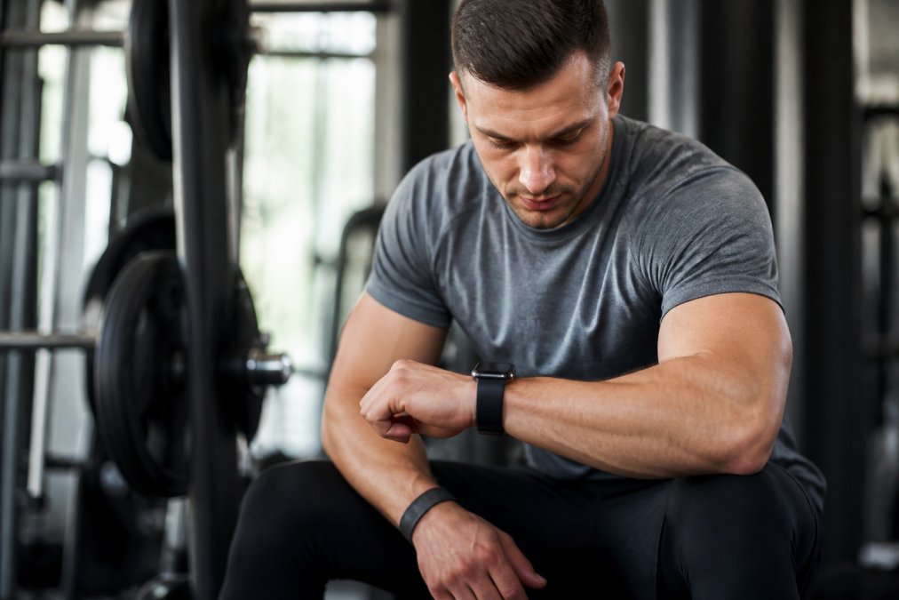 Athlete wearing a smartwatch and fitness tracker during an intense gym session, checking real-time biometric data on the display while performing a strength exercise with focused concentration