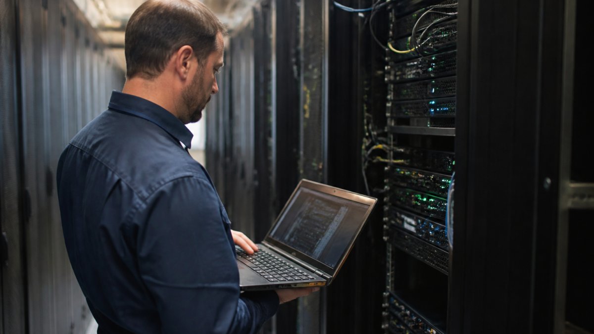 Data center manager using a laptop for remote server management in a rack-filled room