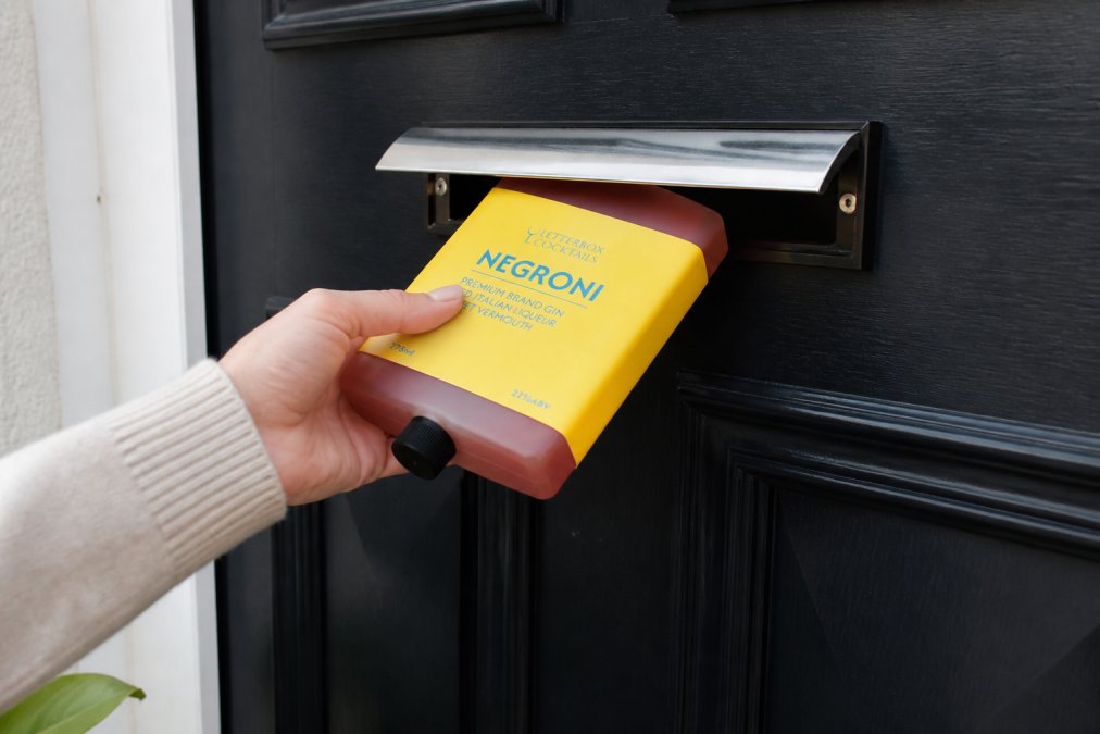 Close-up of a premium cocktail box being placed through a residential letterbox, showing compact packaging design and branded labelling, captured in natural daylight