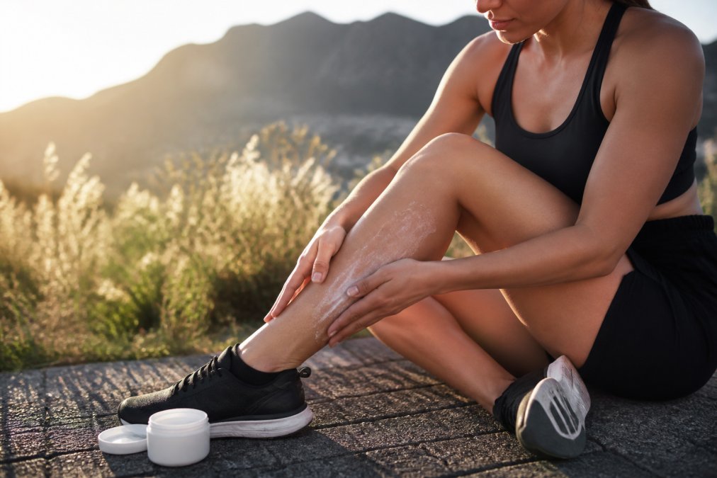 Person massaging their calf muscle after exercise, with magnesium cream visible on skin, suggesting post-workout recovery in bright natural lighting