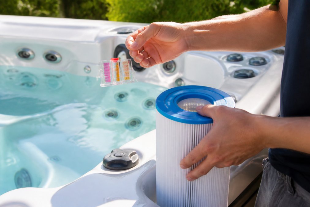 Close-up of hands testing water chemistry with a test kit and checking filters on a hot tub, showing regular maintenance routine in natural daylight