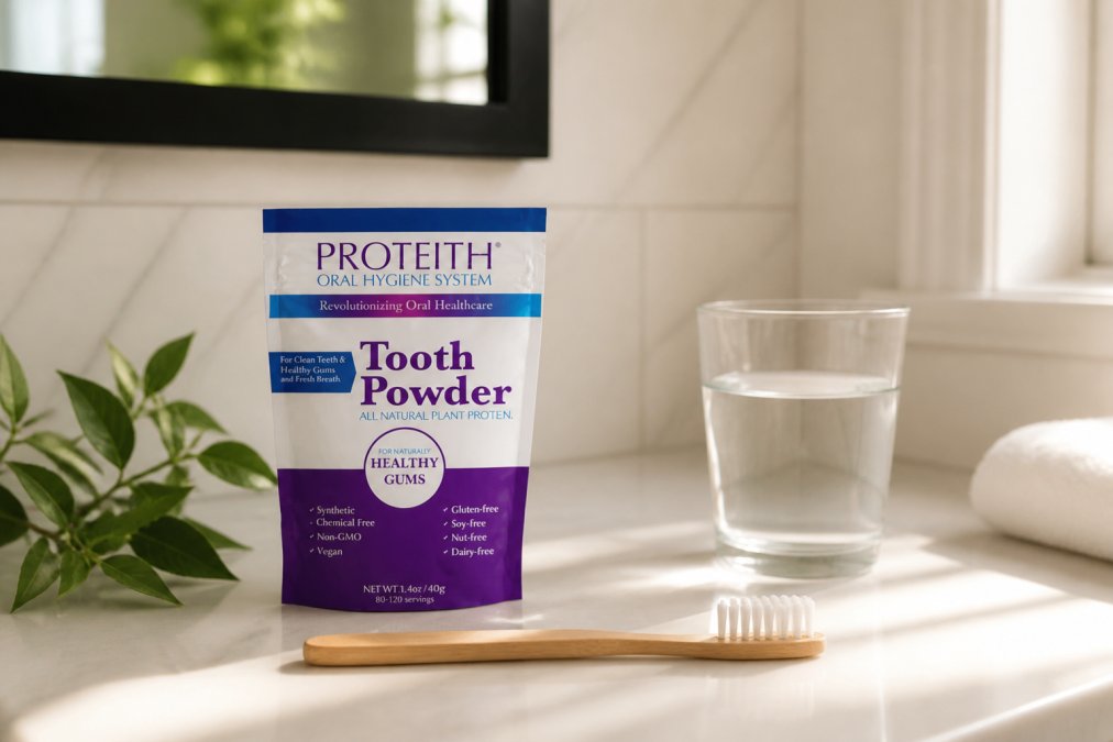 A jar of natural tooth powder on a clean white bathroom counter next to a toothbrush, fresh green leaves, and a glass of water in soft morning light