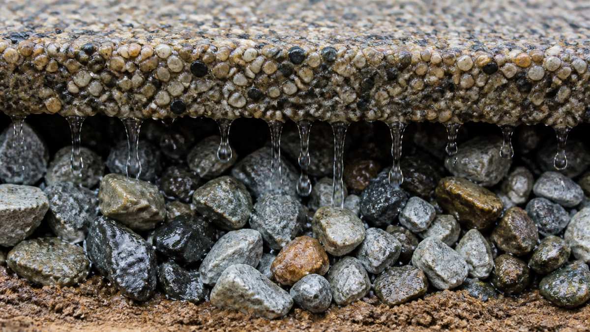 Close-up of water droplets filtering through textured permeable paving surface into gravel sub-base layer below, showing the porous structure and drainage pathway