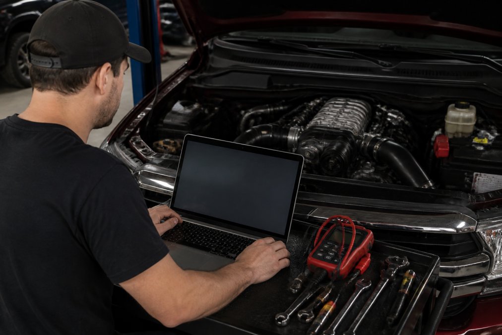 Technician reviewing performance data on laptop screen after supercharger installation, with engine bay visible in background and diagnostic equipment on workbench