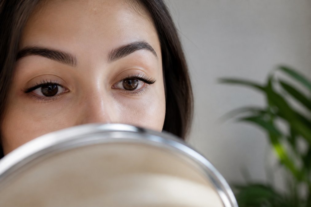 Close-up of a woman's eye with natural-looking press-on lashes applied, soft daylight, mirror reflection visible, minimal makeup, calm expression