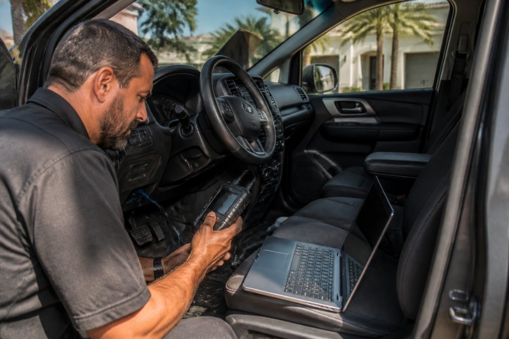 Auto locksmith using a diagnostic tool for car key programming in a sunny Miami driveway