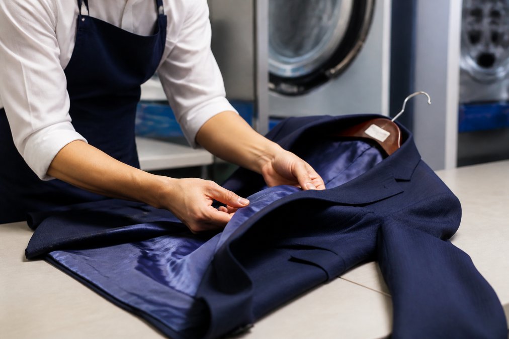 Close-up of hands carefully handling a delicate silk garment or formal blazer being inspected for quality in professional laundry facility with bright, clean lighting