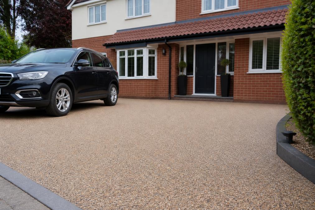 A completed resin bound driveway on a residential property in Norfolk, showing a smooth, uniform surface with a natural stone aggregate finish, a family home in the background, and a car parked on the drive