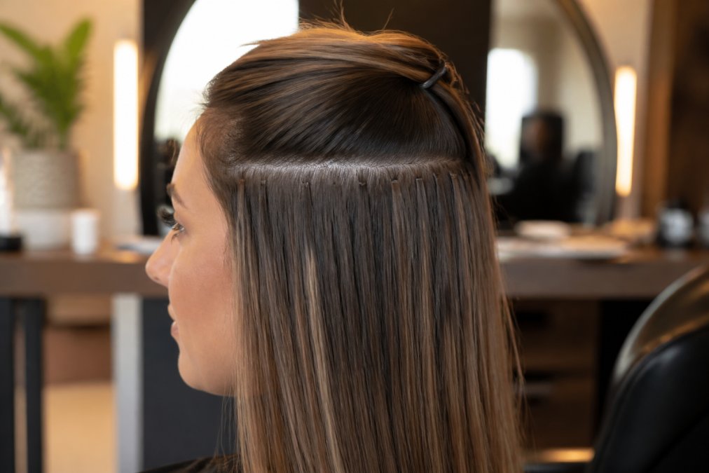 Close-up of a woman with fine, naturally coloured hair showing seamless hair extension placement at the crown, soft natural lighting, salon setting