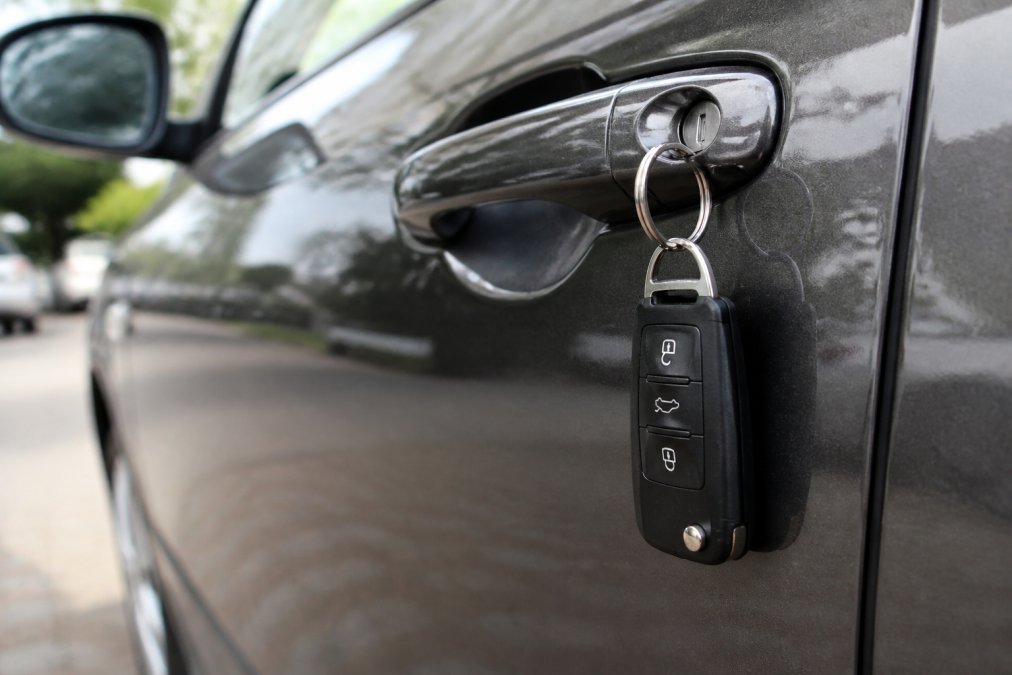 Close-up of a spare car key hanging on a keyring next to a vehicle door handle, showing the practical security benefit of having a backup key readily available