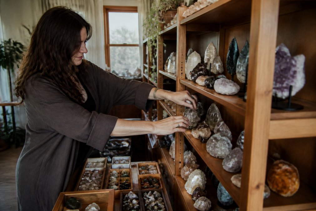 Small business owner arranging crystal carvings in a sunlit studio, supporting neurodivergent led businesses.