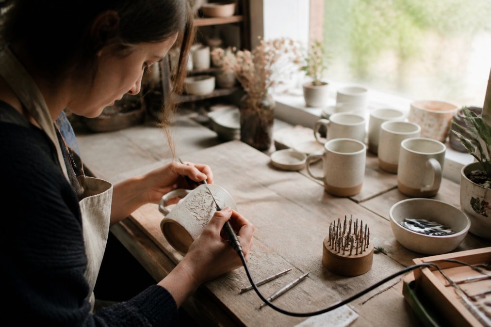 A craftsperson personalizing a handmade product in a sunlit studio typical of small ethical studios.