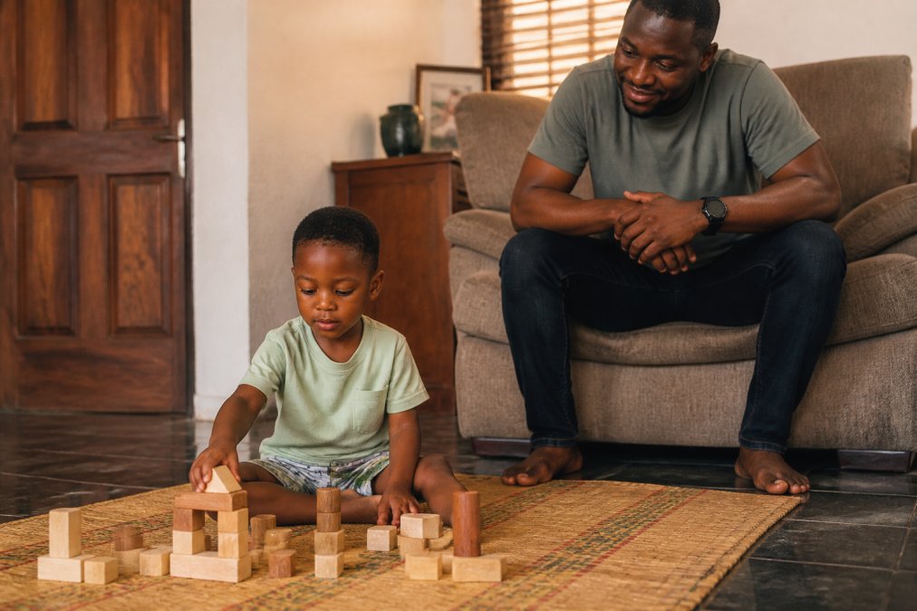 Child engaging in unstructured play with wooden blocks on a mat while a parent watches from nearby