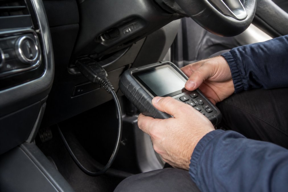 Close-up of professional locksmith hands using advanced key programming equipment on a vehicle's diagnostic port, modern car interior visible