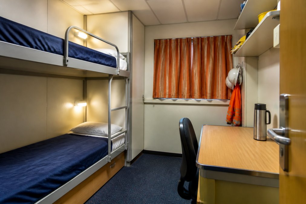 A clean, modern offshore accommodation cabin with a bunk bed, small desk, and personal storage, showing a worker's home away from home on an oil platform