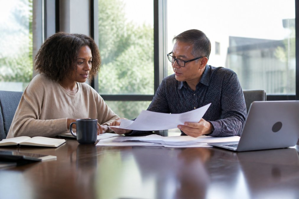 A business owner reviewing financial documents with an advisor at a modern conference table, laptop and tax forms visible, natural light from large windows