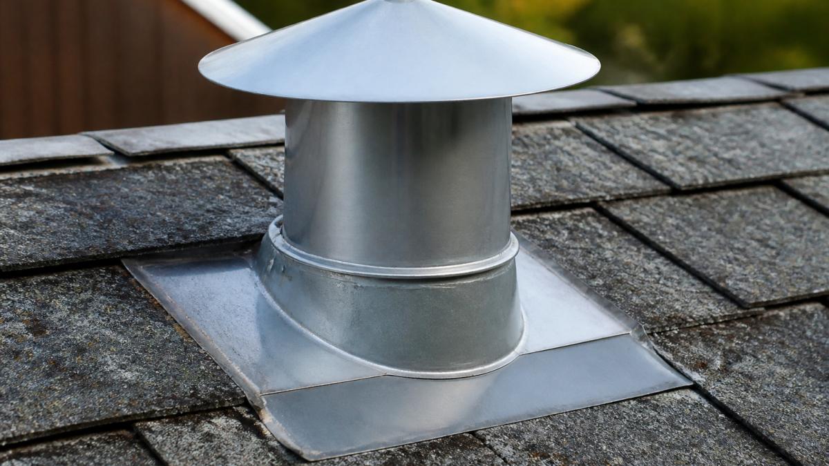 Close-up of a metal pipe cap installed on a roof, showing proper sealing and overlap with surrounding flashing materials and weathered shingles