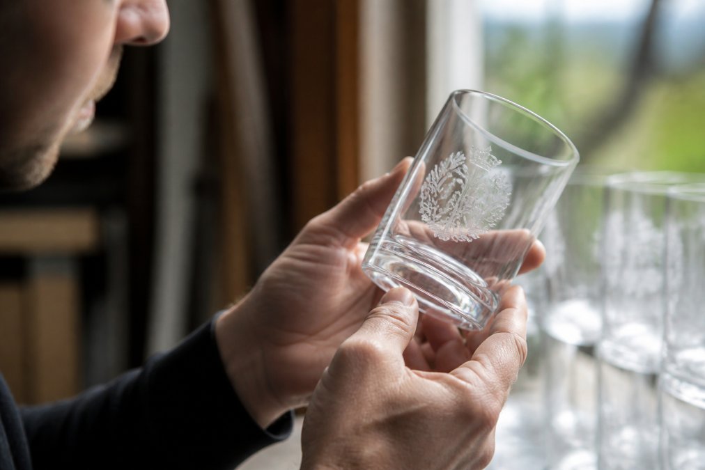 Close-up of hands carefully examining etched logo detail on branded glass, natural window lighting showing clarity and precision of customisation work