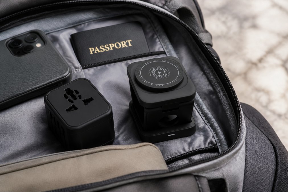 A traveler's backpack open with a foldable wireless charger nestled between a passport, travel adapter, and phone case, demonstrating compact portability in realistic travel conditions with natural daylight