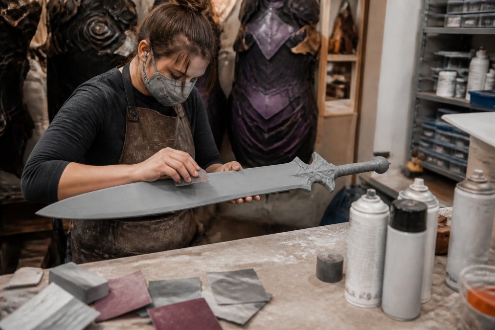 Cosplayer sanding and priming 3D printed props on a workbench in a workshop filled with finishing tools