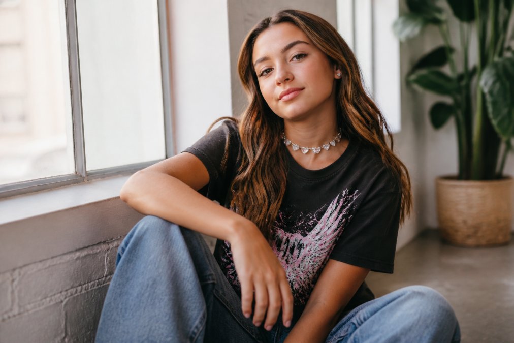 Teen girl wearing a crystal heart choker with clear stud earrings, styled with a casual graphic tee and baggy jeans, posed confidently with natural window lighting