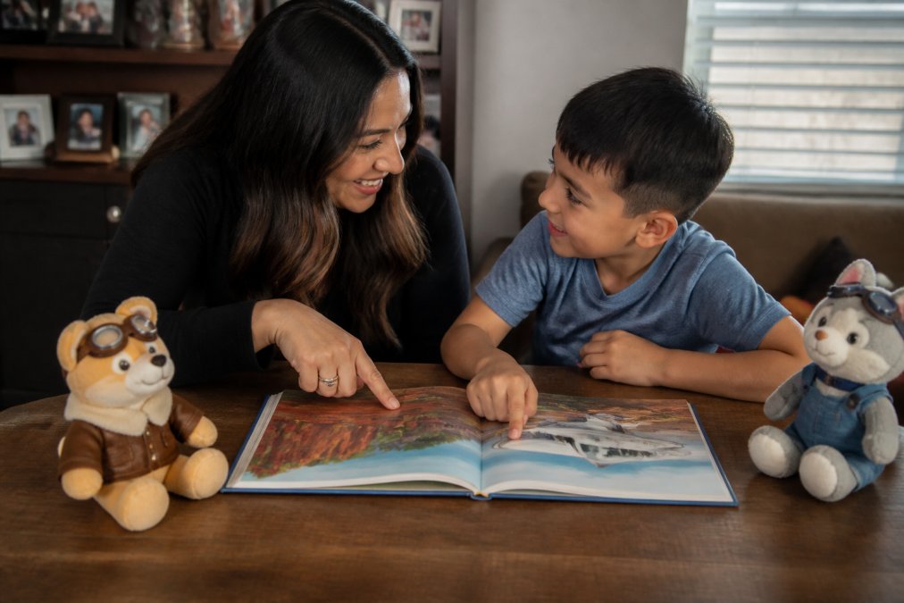 A parent and child sitting together at a cozy table, both leaning in toward an open adventure book with colorful illustrations, pointing excitedly at a scene in the story while smiling at each other
