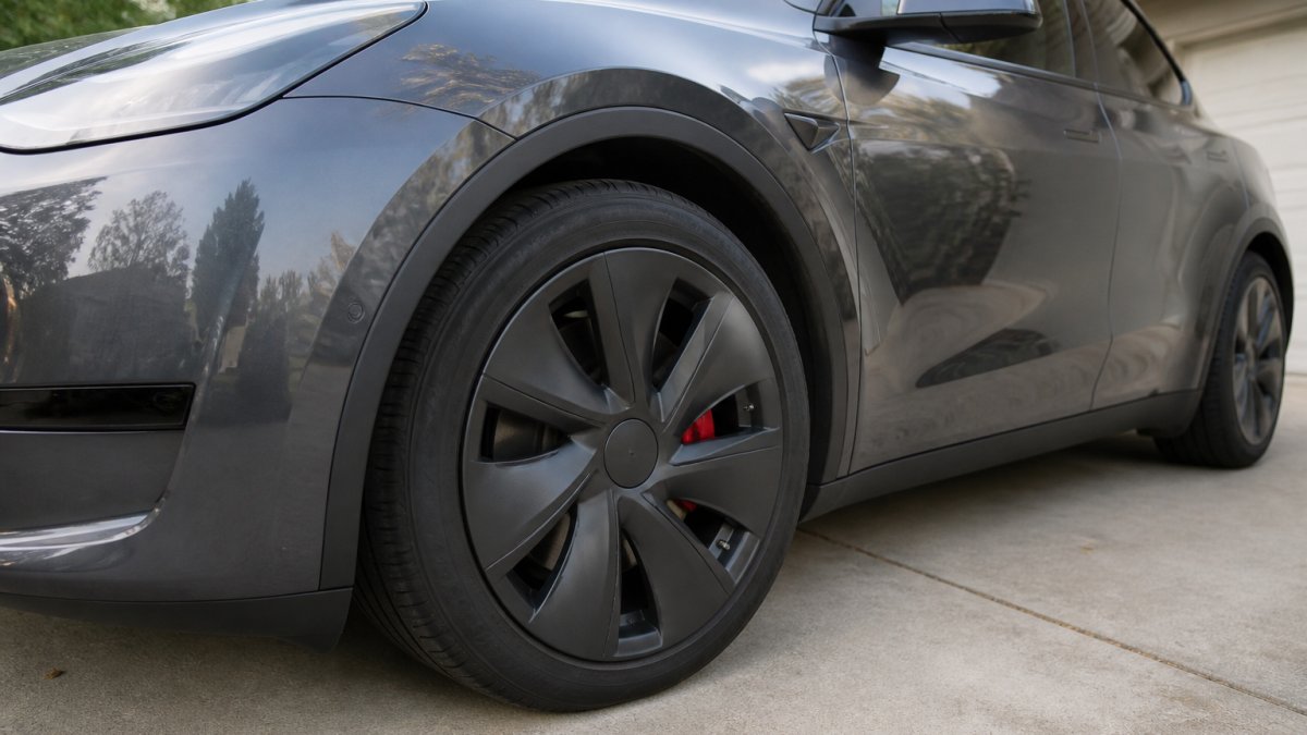 Close-up of a modern electric SUV parked in a driveway, showing a clean aero-style wheel cover on one wheel with the tire and brake caliper visible behind it