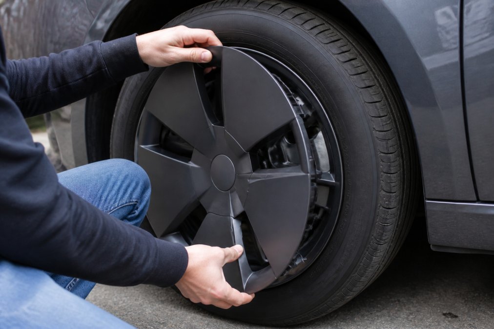 Close-up of hands aligning and securing a clip-on aerodynamic wheel cover onto an electric vehicle wheel, showing the attachment mechanism and proper positioning