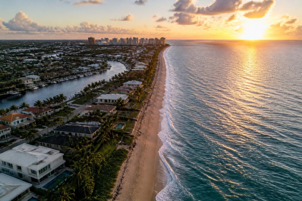 Best Affordable Beach Towns to Live in USA: 2026 Guide 1 Aerial view of a scenic coastal town with sandy beaches, colorful beach houses, waterfront properties, and palm trees lining the shore at golden sunset, with gentle waves rolling onto the sand