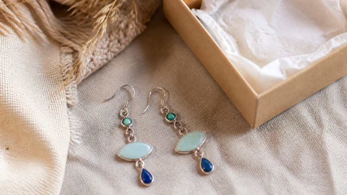 Handmade dangle earrings displayed on linen next to a gift box and tissue paper in warm sunlight