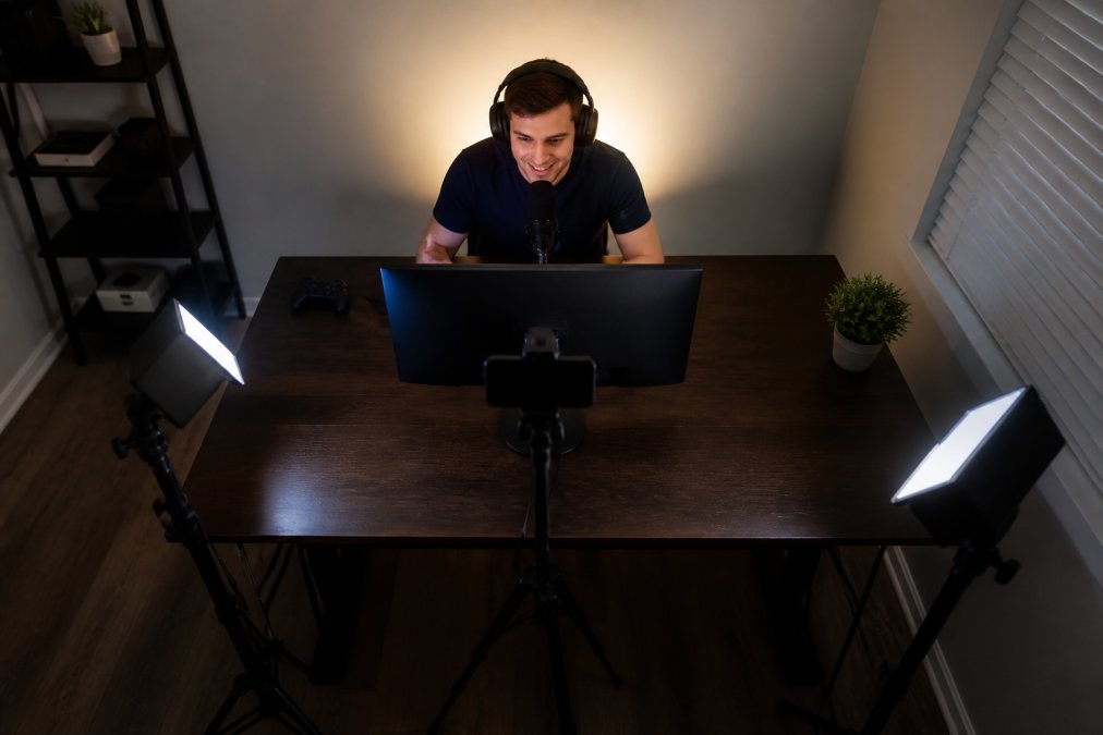 Overhead view of streaming desk setup with three light sources positioned around monitor: key light at 45-degree angle left of camera, fill light right side at lower intensity, backlight behind monitor pointing at wall, all angles and distances clearly visible