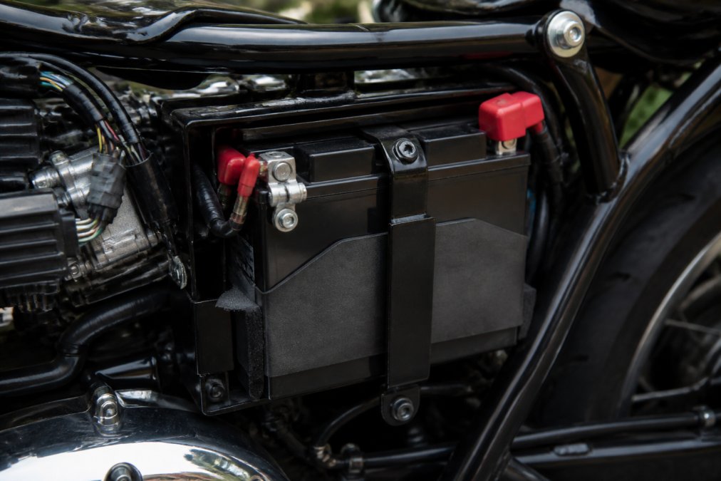 Close-up of a touring motorcycle battery mounted in engine bay, showing sealed AGM construction, terminal connections, and vibration dampening materials visible through the case
