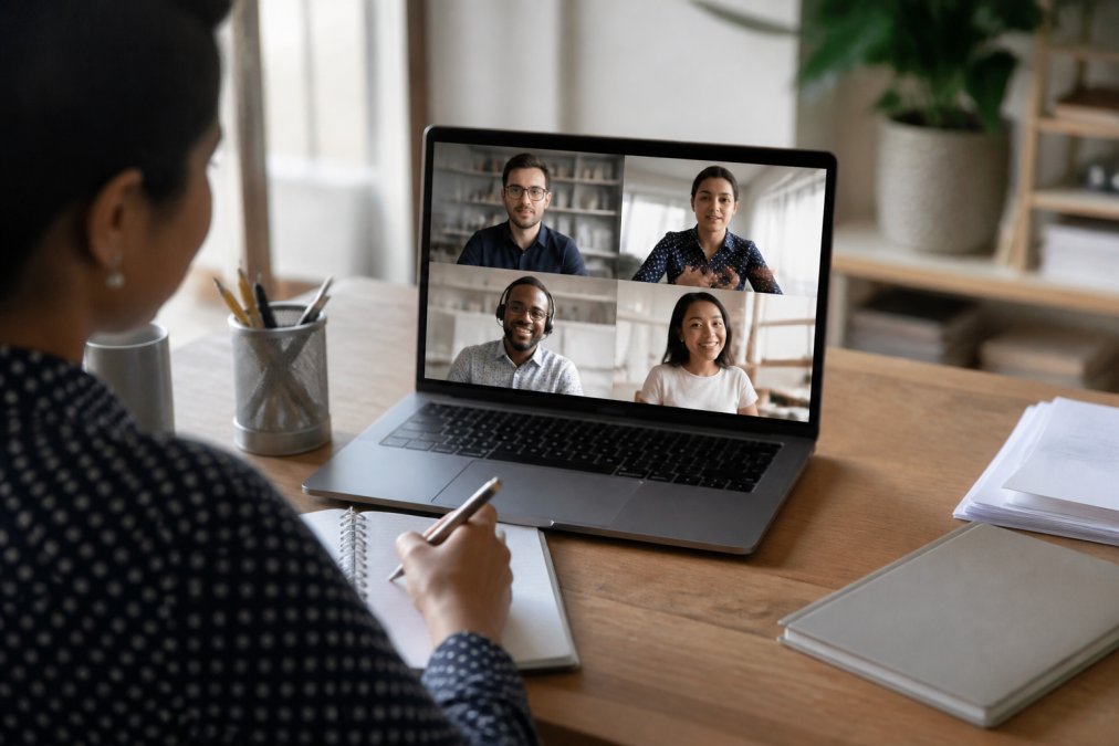 Team of professionals in a video conference call on a laptop screen, with one person taking notes on a notepad