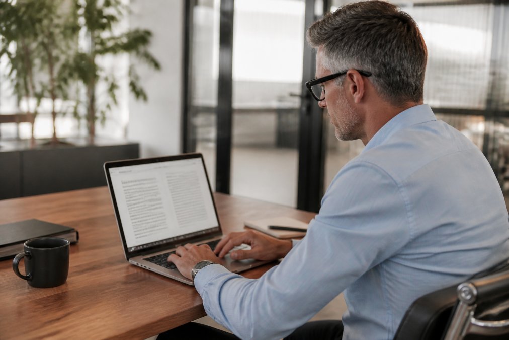 A sales manager reviewing meeting notes and analytics on a laptop in a bright, modern office with a coffee cup nearby