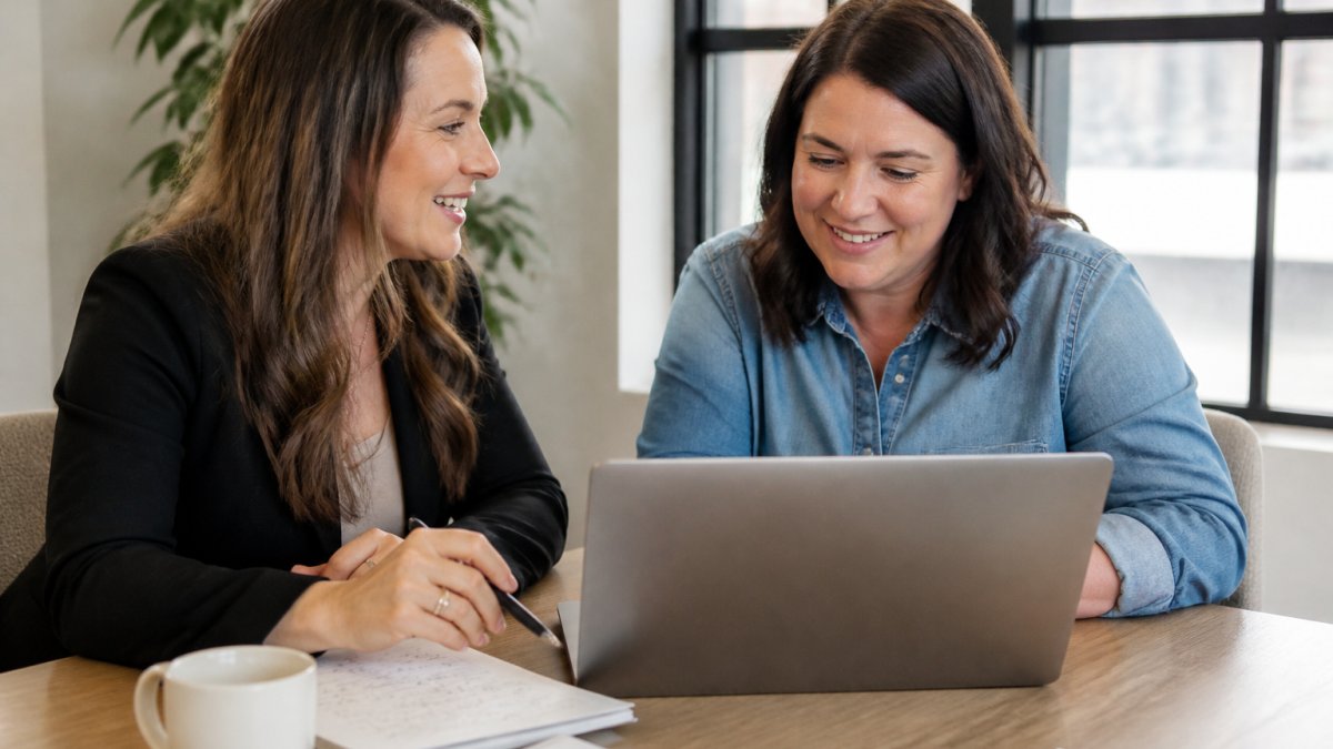 A consultant and a small business owner reviewing a custom CRM dashboard on a laptop in a bright office, with handwritten notes and a coffee cup on the table