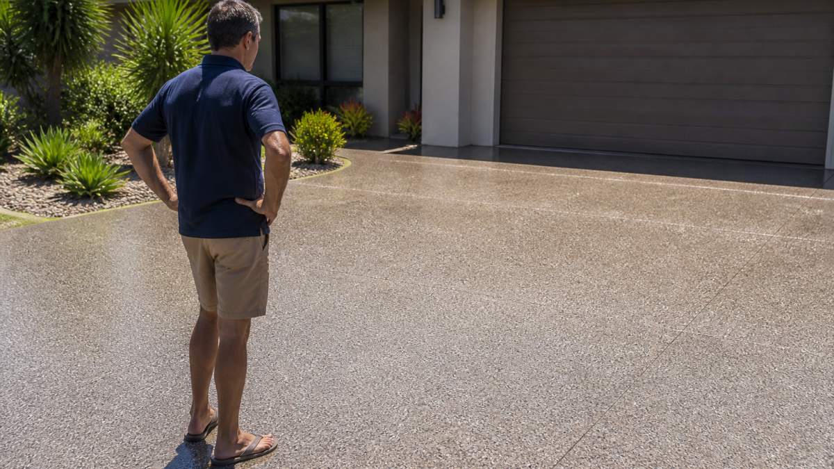 Homeowner inspecting the texture and color of a newly resurfaced driveway as one of the best alternatives to standard